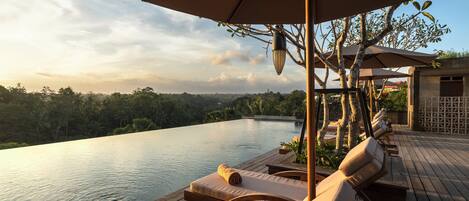A wooden deck with lounge chairs and umbrellas overlooking a pool.