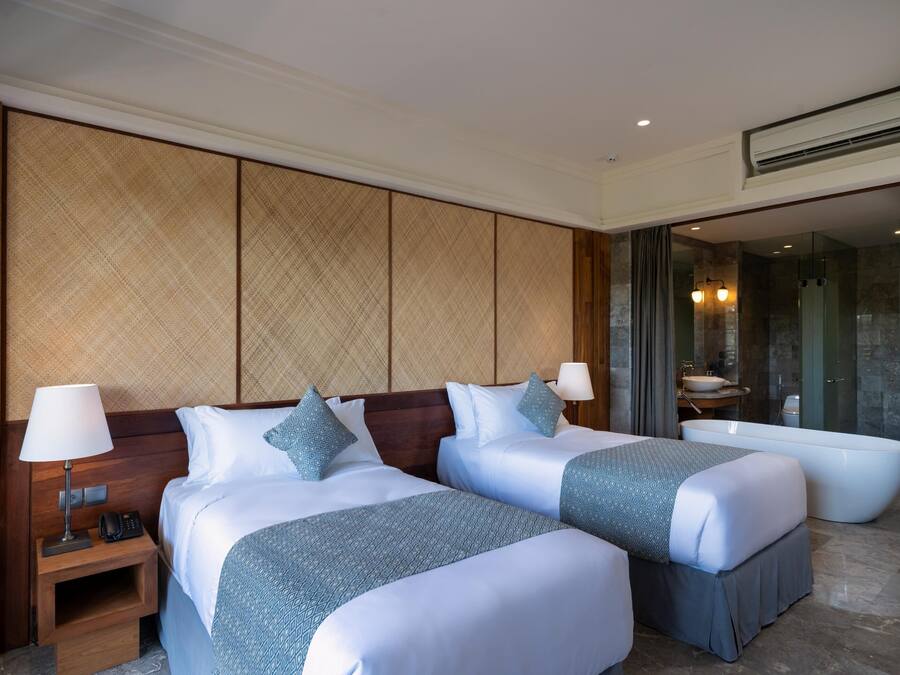 A hotel room with two beds, a large bathtub, and a separate bathroom with a sink and mirror.