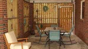Un espace patio avec une table et des chaises en bois, un fauteuil rembourré et un mur en briques.
