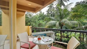 A balcony with a glass table, wicker chairs, and a view of tropical vegetation. - Alaya Stays Veera Strand Park (Calangute)