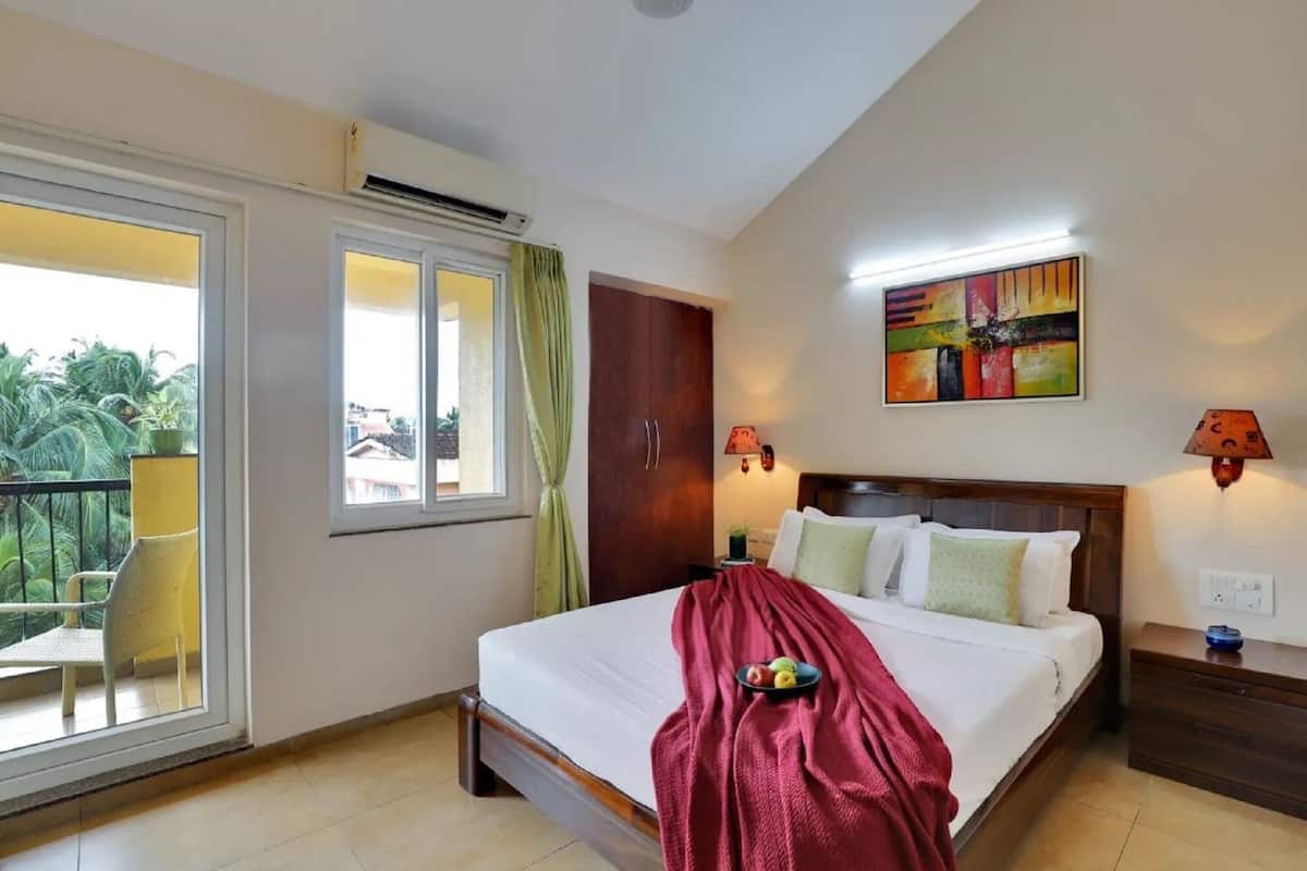 A hotel room with a bed, a nightstand, a lamp, a window with curtains, a balcony with a chair, and a painting on the wall.
