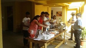 A communal dining area with a long table set for a meal, surrounded by people. - Alaya Stays Veera Strand Park (Calangute)