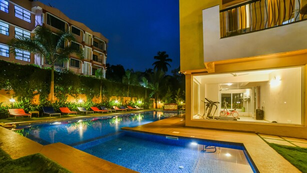 A swimming pool with lounge chairs, a fitness area, and a building with a balcony. - Alaya Stays Veera Strand Park (Calangute)