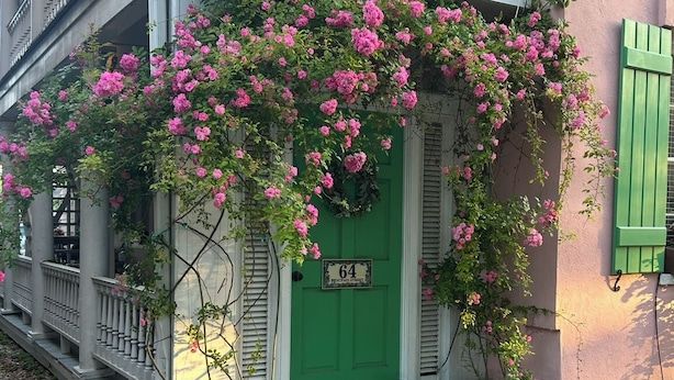 A building with a green door, a balcony with white railings, and pink flowers.