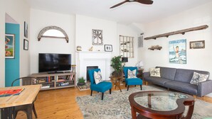 A living room with a television, two blue armchairs, a grey sofa, a wooden coffee table, and a ceiling fan.