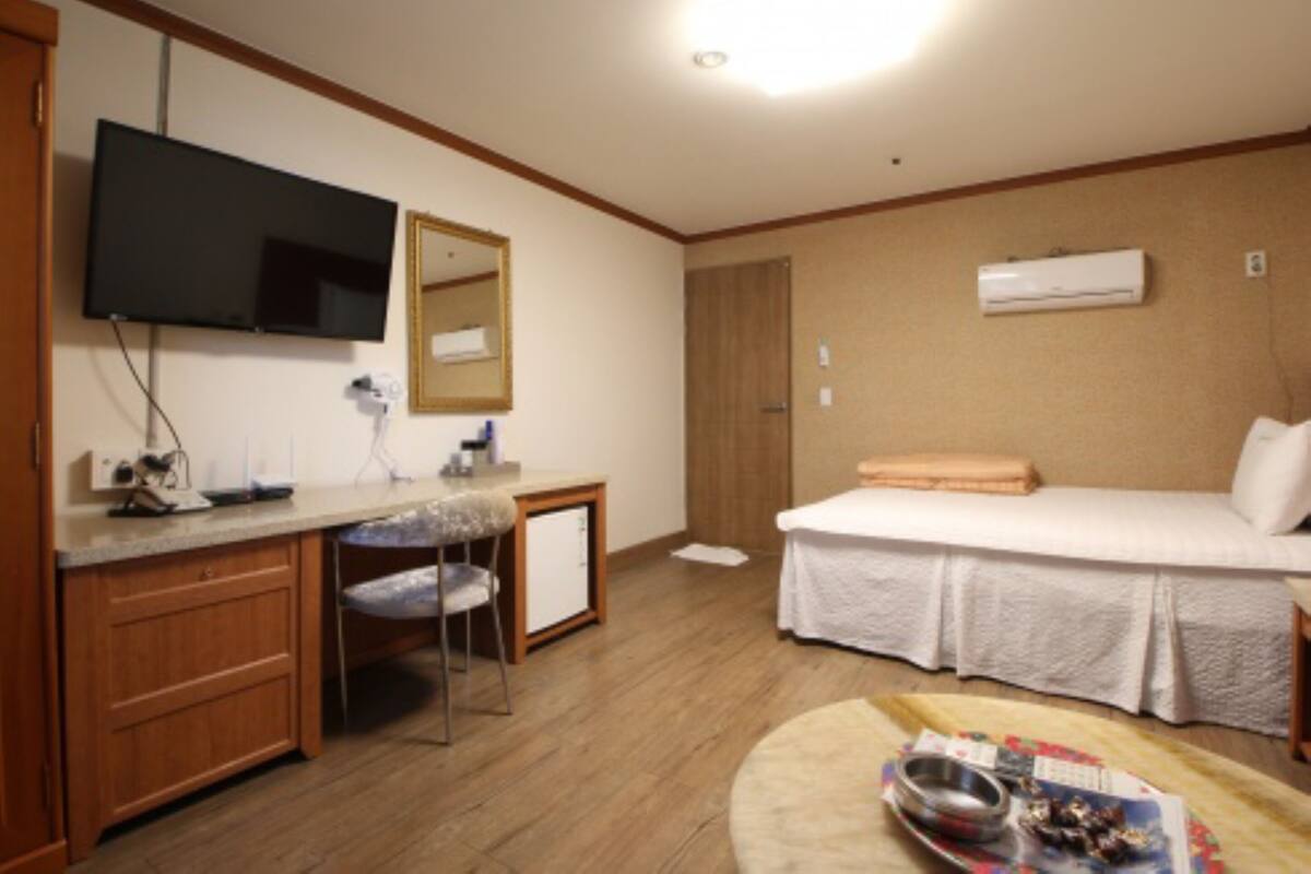 A hotel room with a bed, a desk with a chair, a television, and an air conditioning unit.