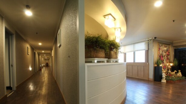 A hotel hallway with wooden flooring, a curved wall with a plant display, and a decorative area with statues and plants. - Yangji Park Hotel (Changwon)