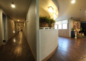 A hotel hallway with wooden flooring, a curved wall with a plant display, and a decorative area with statues and plants. - Yangji Park Hotel (Changwon)