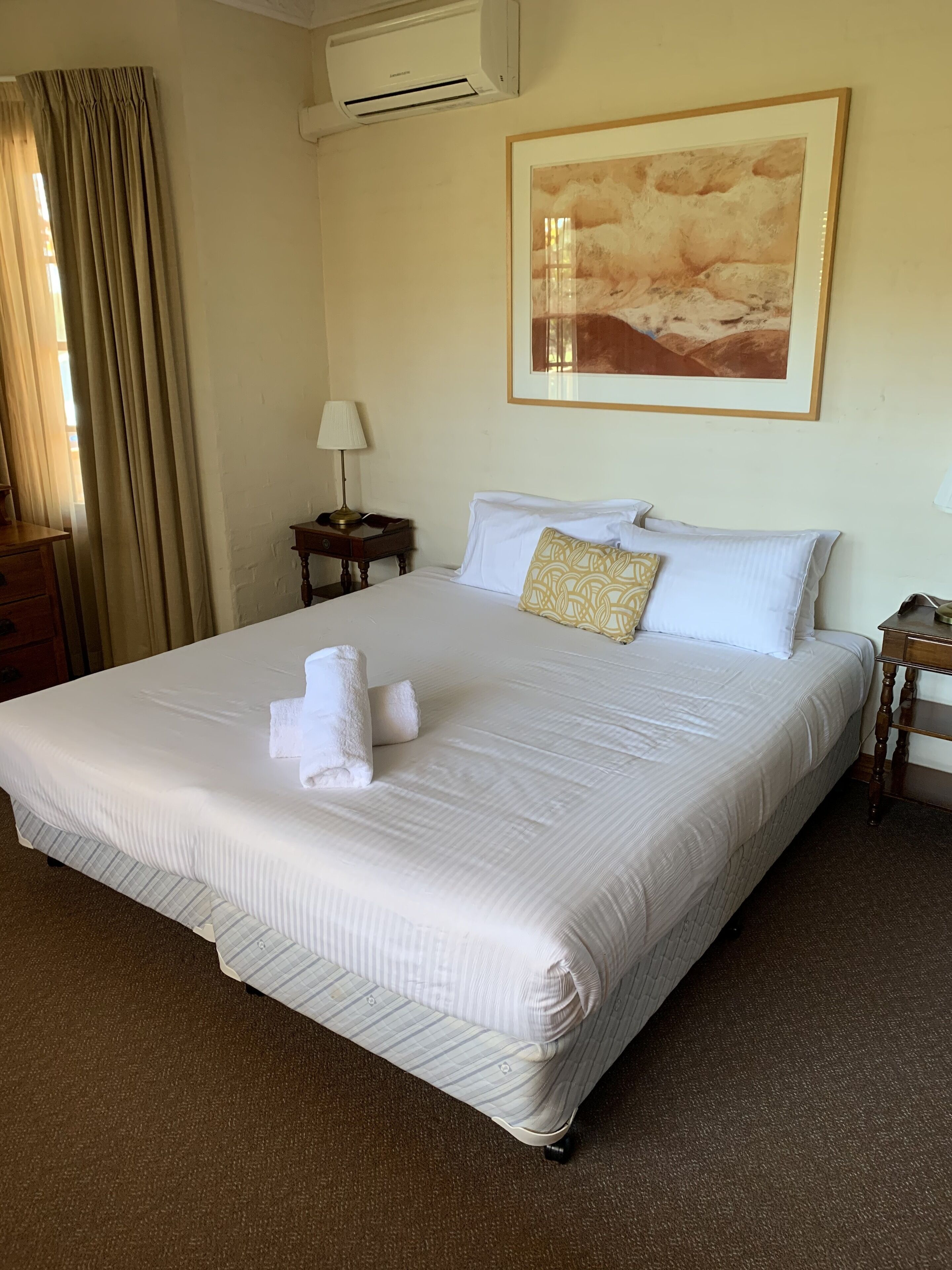 A neatly made bed with white linens and a decorative pillow, a bedside lamp, and a framed artwork on the wall.