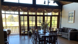 Un comedor amplio con una mesa y sillas de madera, ventanas grandes que ofrecen vistas al exterior, y un rincón de estar acogedor con un sofá.