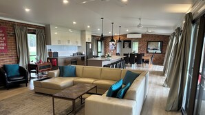 Una sala moderna con un amplio sofá modular color beige, una mesita de centro y un comedor, con una cocina al fondo.