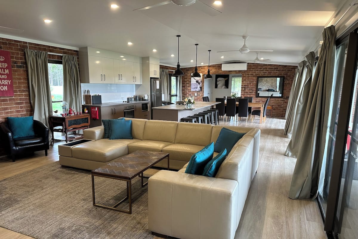A modern living room with a large beige sectional sofa, a coffee table, and a dining area with a kitchen in the background.