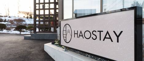 A sign with the word "HAOSTAY" and a logo, placed in front of a building with large windows and a modern design.