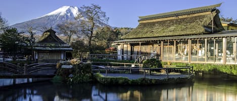 A traditional Japanese building with a thatched roof, a wooden bridge, and a reflection in the water.