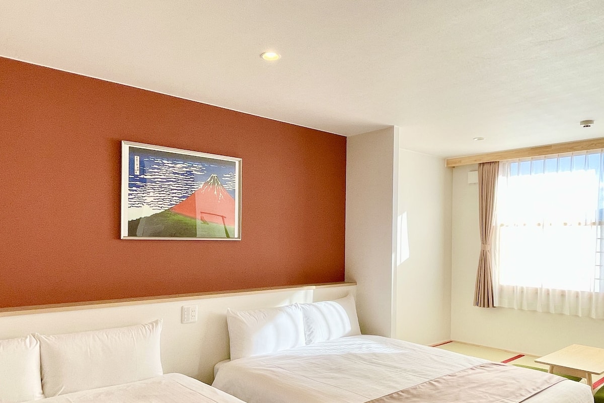 Quarto de hotel com duas camas, um quadro na parede, uma janela com cortinas e uma mesinha.