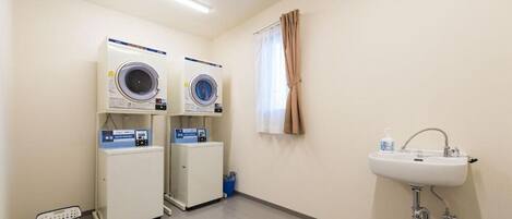 Una lavandería con dos lavadoras, un lavabo y una ventana con cortinas.