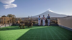 A rooftop with a view of a mountain, a wooden table, and two people in traditional attire. - HaoSTAY (Fujikawaguchiko)
