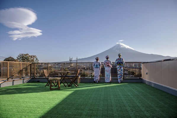 A rooftop with a view of a mountain, a wooden table, and two people in traditional attire.