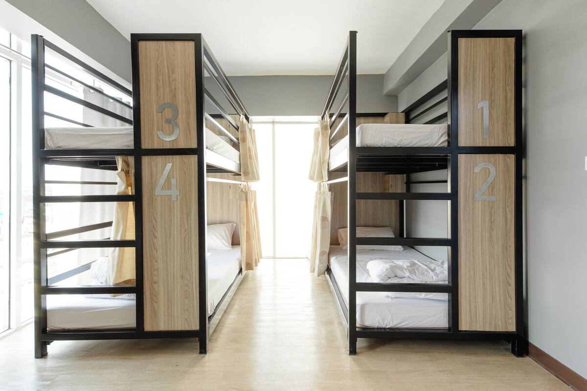 A corridor with bunk beds labeled 1, 2, 3, and 4, leading to a bright room with a large window.