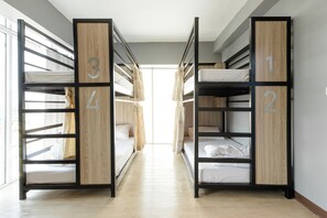 A corridor with bunk beds labeled 1, 2, 3, and 4, leading to a bright room with a large window. - Sleep To Fly Hotel & Hostel (Bangkok)