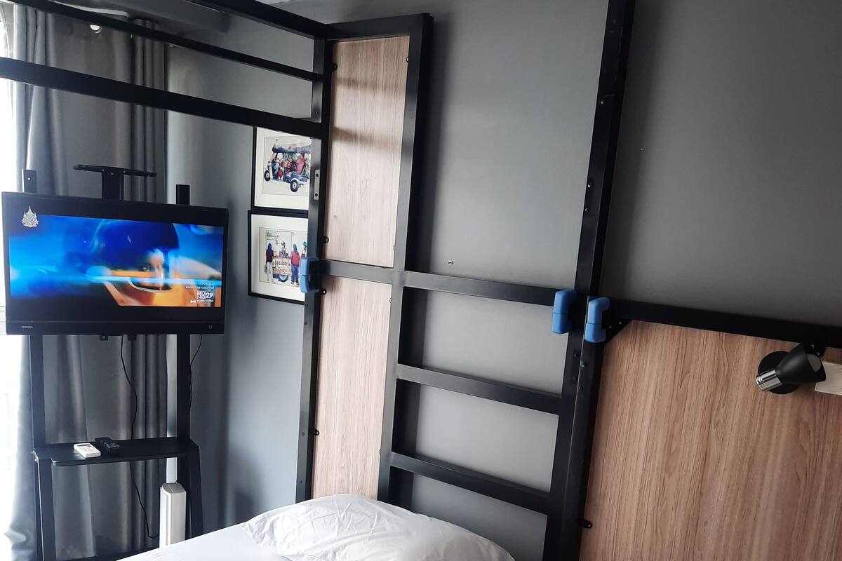 A hotel room with two beds, a TV on a stand, and a wall-mounted shelf with pictures.