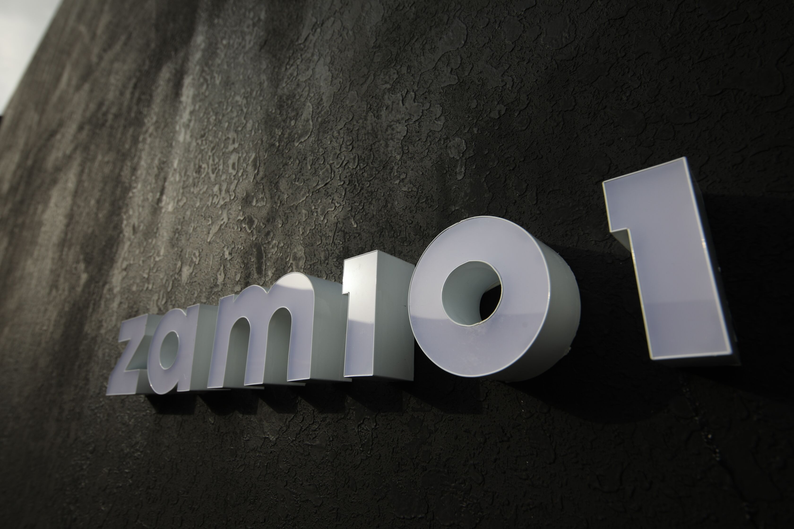 A metallic sign with the text "zam101" on a textured wall.