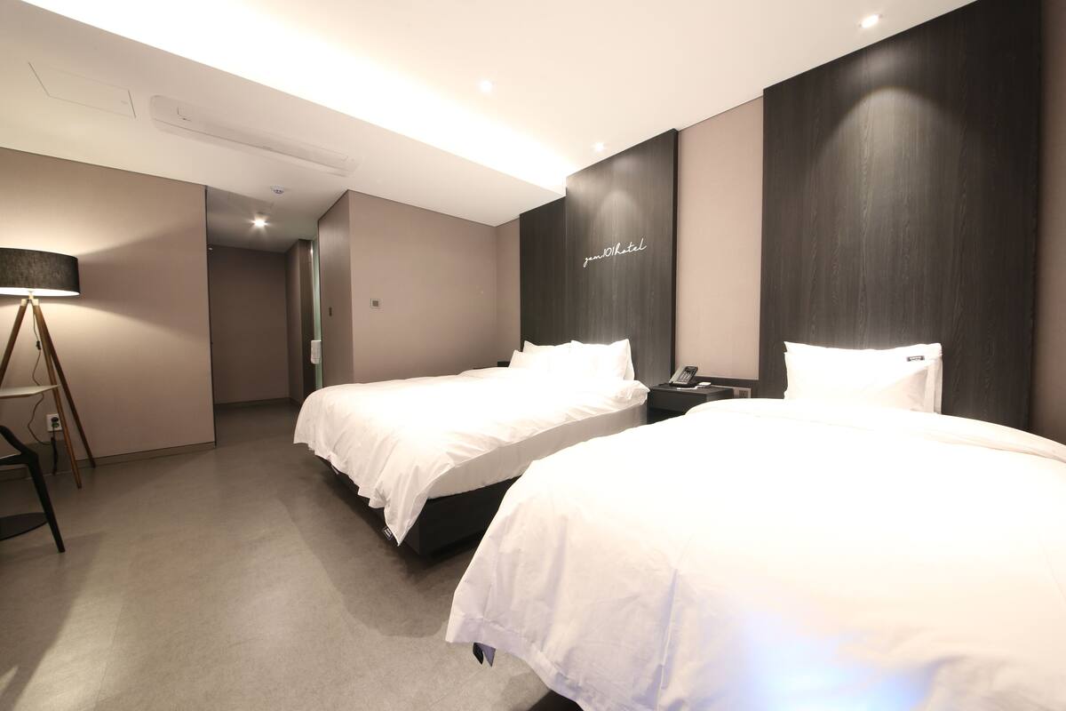A modern hotel room with two beds, a desk, and a lamp.