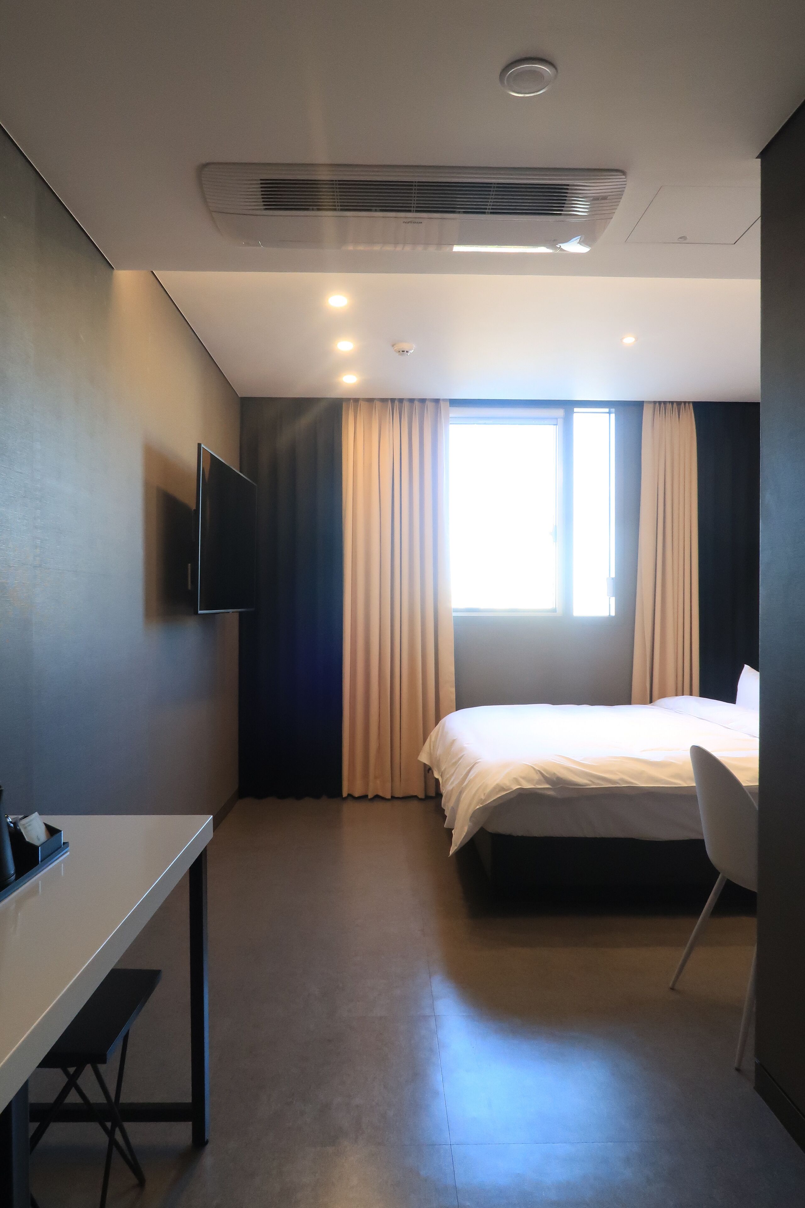 A modern hotel room with a bed, a desk, and a TV.