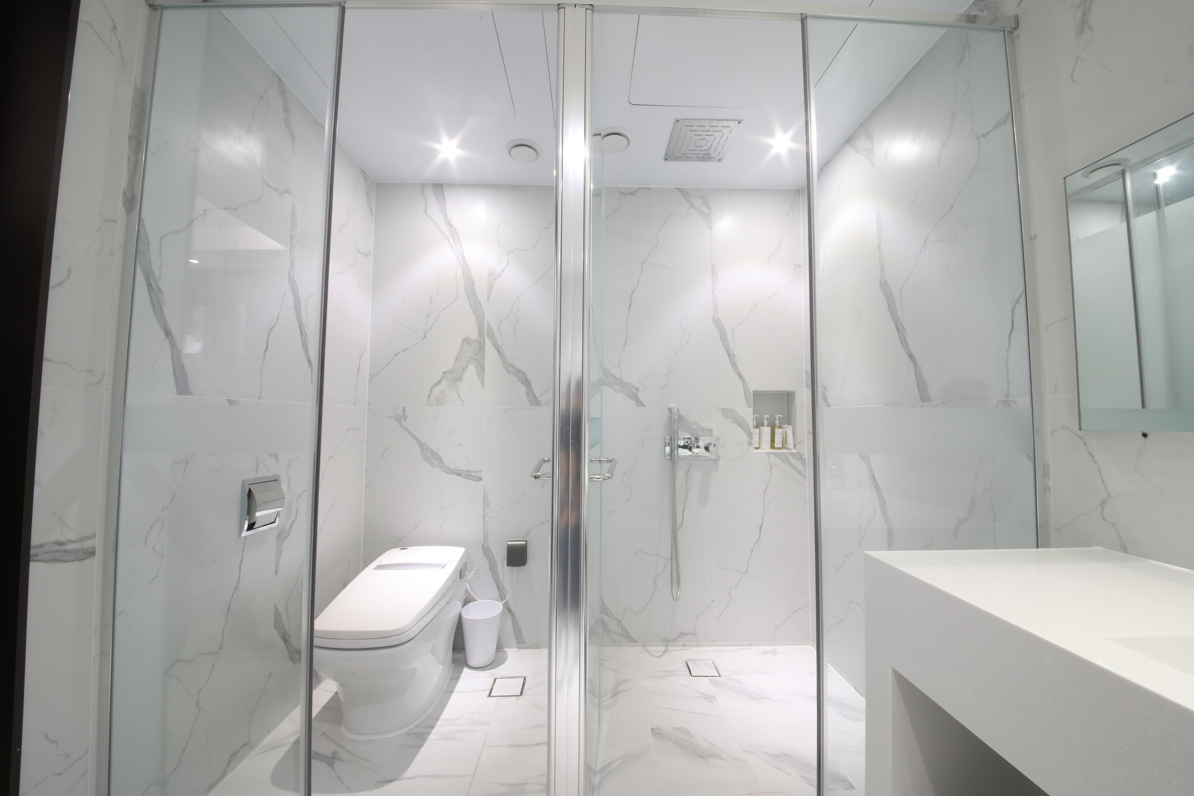 A modern bathroom with a glass-enclosed shower, a white toilet, and a marble-tiled floor.
