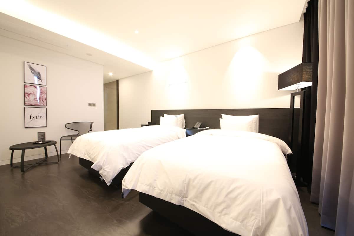 A hotel room with two beds, a desk, a chair, and artwork on the wall.