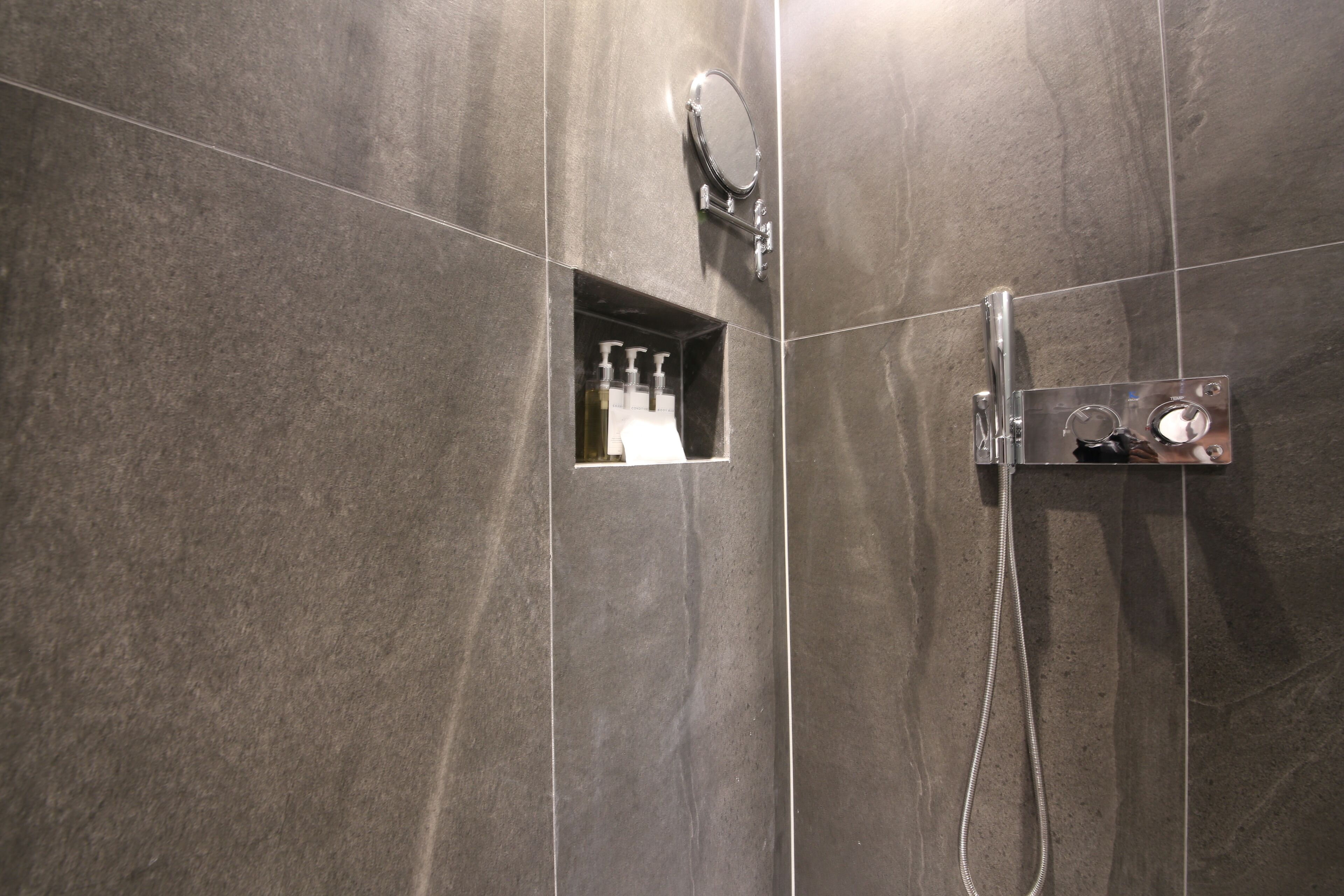 A modern bathroom with a shower, a mirror, and a soap dispenser.
