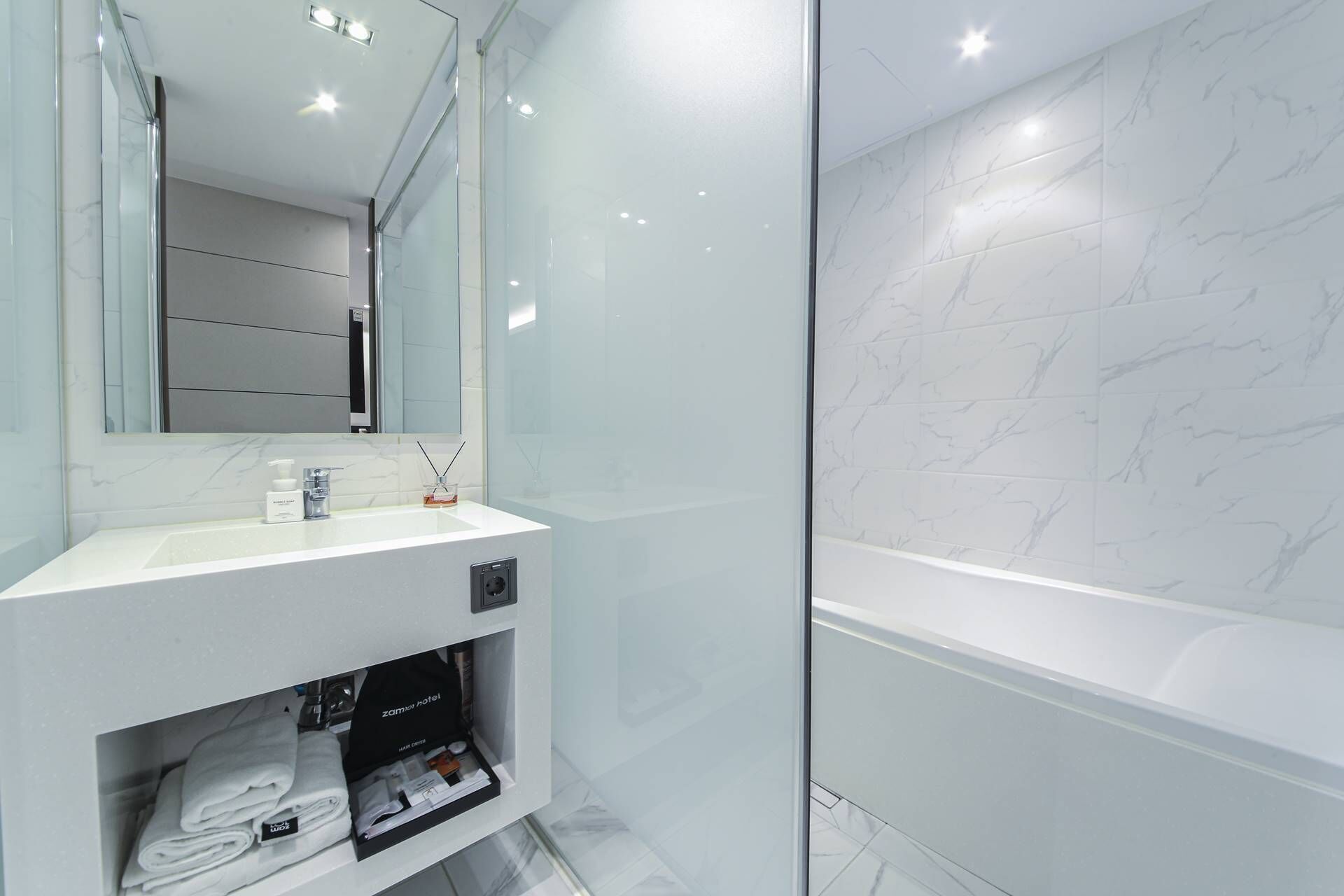 Un baño moderno con pared de mármol blanco, cabina de ducha de vidrio y tocador con espejo.
