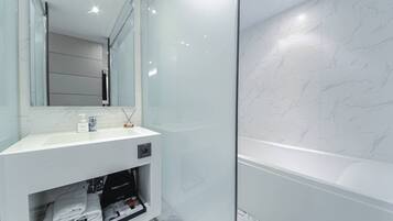 Un baño moderno con pared de mármol blanco, cabina de ducha de vidrio y tocador con espejo.