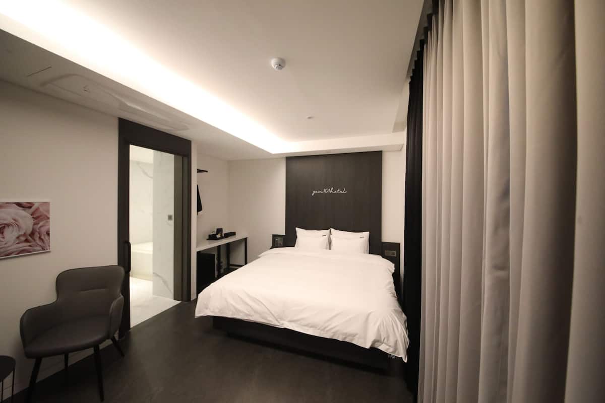 A modern hotel room with a large bed, a desk, and a chair.