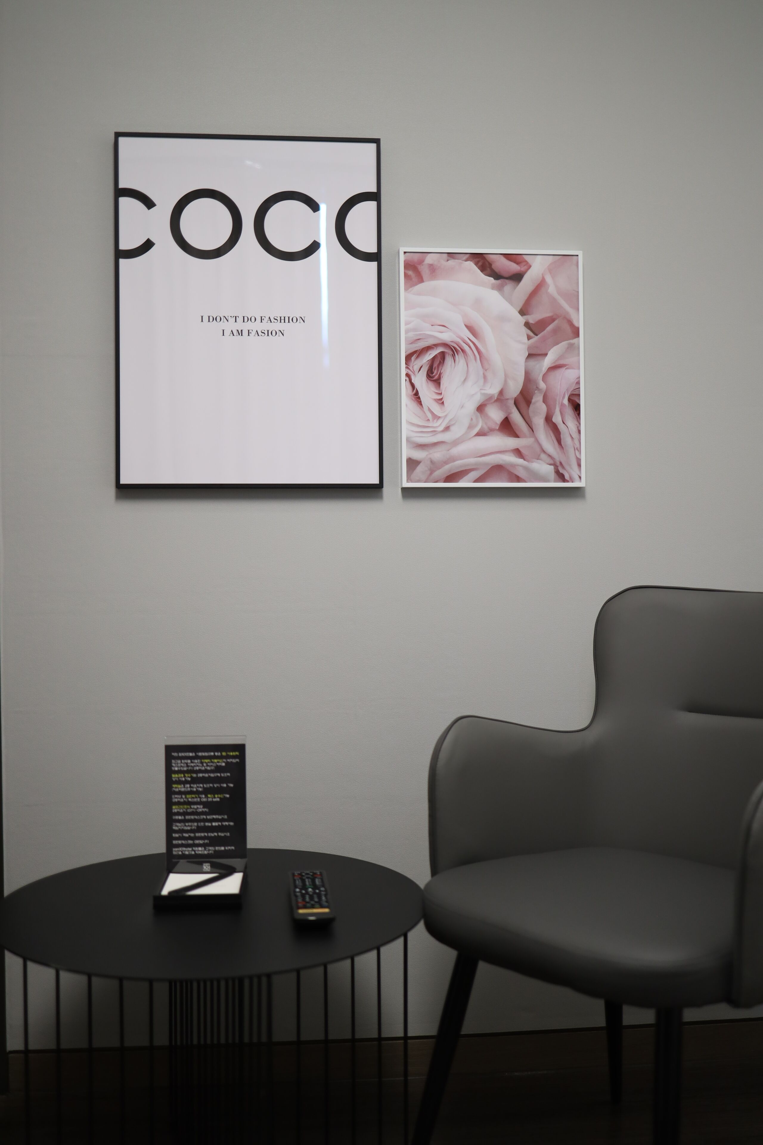 A framed poster with the word "COCO" and a quote, a framed floral artwork, a small table with a remote control, and a modern chair.