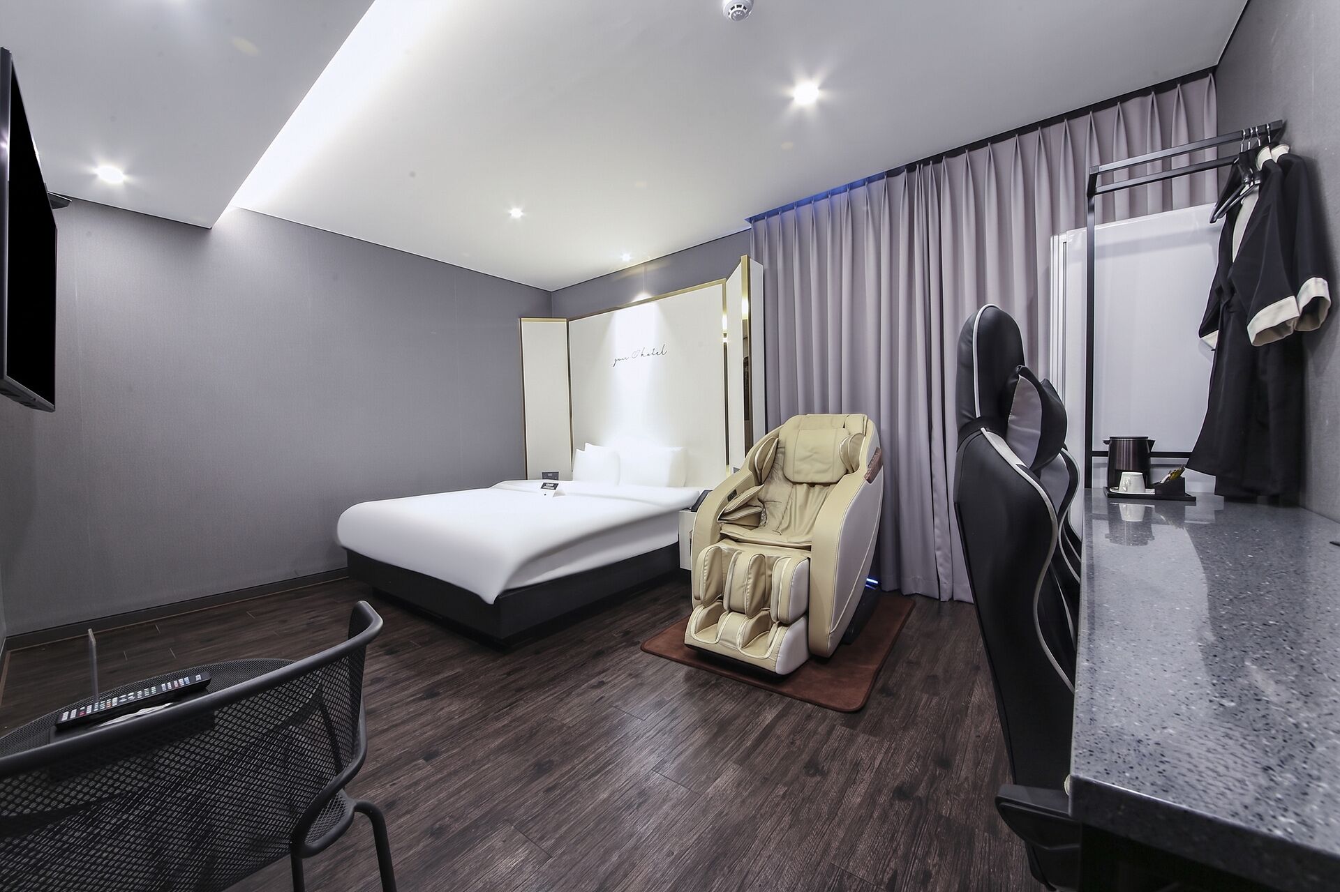 Una habitación de hotel moderna con cama, sillón de masaje, escritorio y un espejo grande.