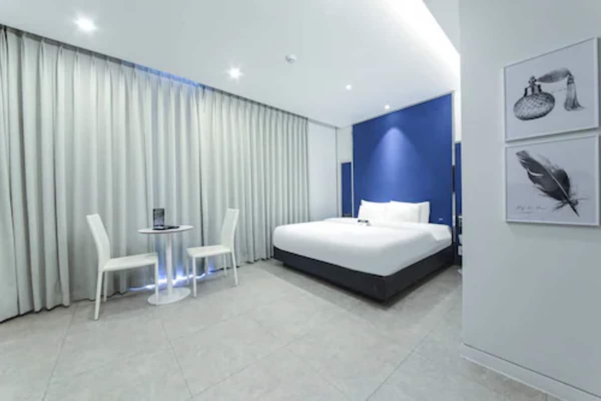 A modern hotel room with a large bed, a small round table, two white chairs, and a view of the city.
