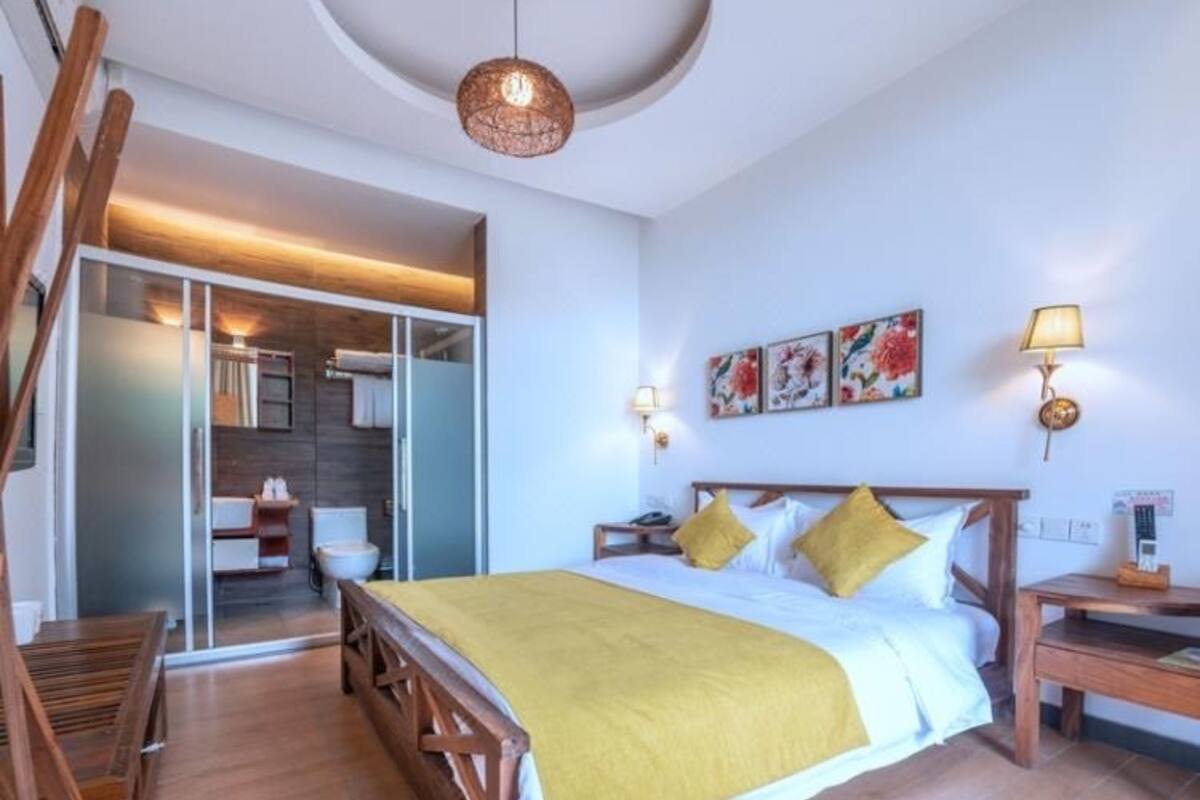 Une chambre avec un lit en bois, un banc, un bureau et une chaise. On y trouve un luminaire au plafond et une lampe fixée au mur.