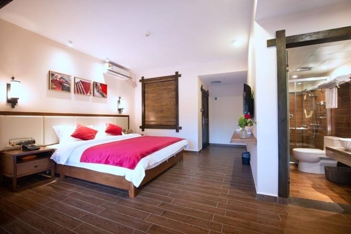Une chambre à coucher avec un lit en bois, une table de chevet, un climatiseur fixé au mur et une salle de bain dotée d’une cabine de douche en verre.
