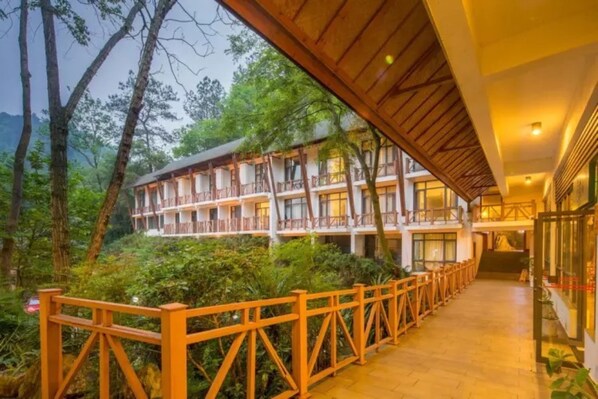 Un hotel con una galería techada, varios balcones y abundante vegetación que rodea el edificio.