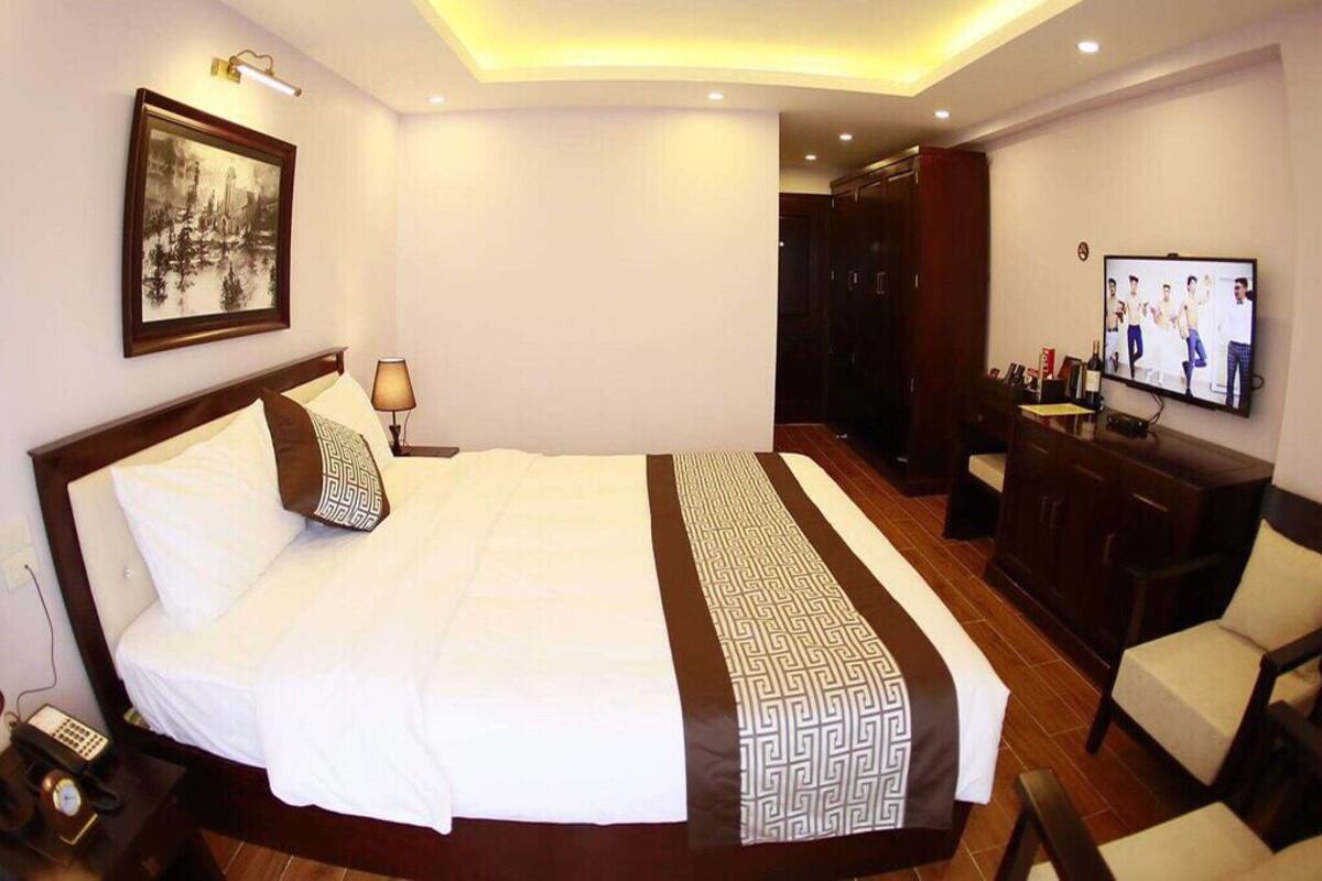 Een hotelkamer met een groot bed, bedlampen, een televisie, een bureau met stoel en een kledingkast.