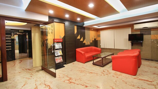 A lobby with a glass elevator, red seating, a coffee table, and a wall-mounted TV. - OYO 4439 Aura Inn (Bengaluru)