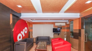 A modern lounge area with a large red logo, leather sofas, a glass coffee table, and a flat-screen TV. - OYO 4439 Aura Inn (Bengaluru)