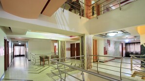 A multi-level hotel corridor with a central staircase, handrails, and patterned flooring. - OYO 4439 Aura Inn (Bengaluru)