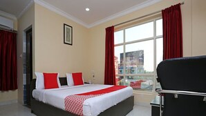 A hotel room with a bed, a black chair, a window with red curtains, and a framed picture on the wall. - OYO 4439 Aura Inn (Bengaluru)