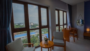 A hotel room with large windows, a wooden table, two chairs, and a small round table with a flower vase. - Stellar Hotel (Phu Quoc)