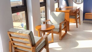 A room with large windows, a wooden dining table, and two wooden chairs with cushions. - Stellar Hotel (Phu Quoc)