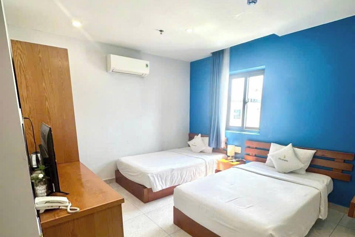 Habitación de hotel con dos camas, un escritorio de madera, un teléfono y una ventana con cortinas azules.