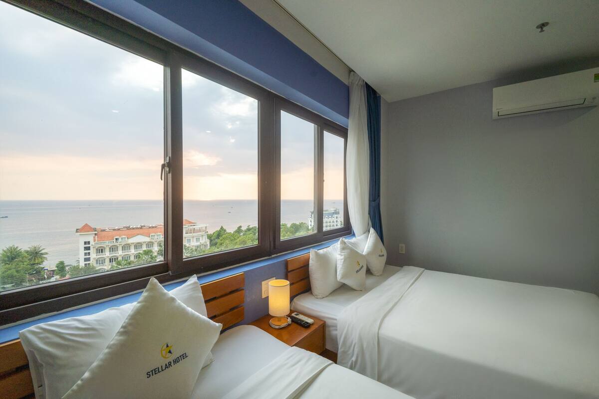 Habitación de hotel con dos camas, vista al mar y una ventana con cortinas.