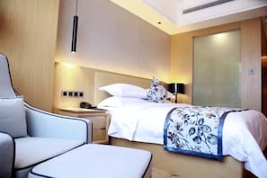 A modern hotel room with a bed, a nightstand, a chair, and a bedside table.